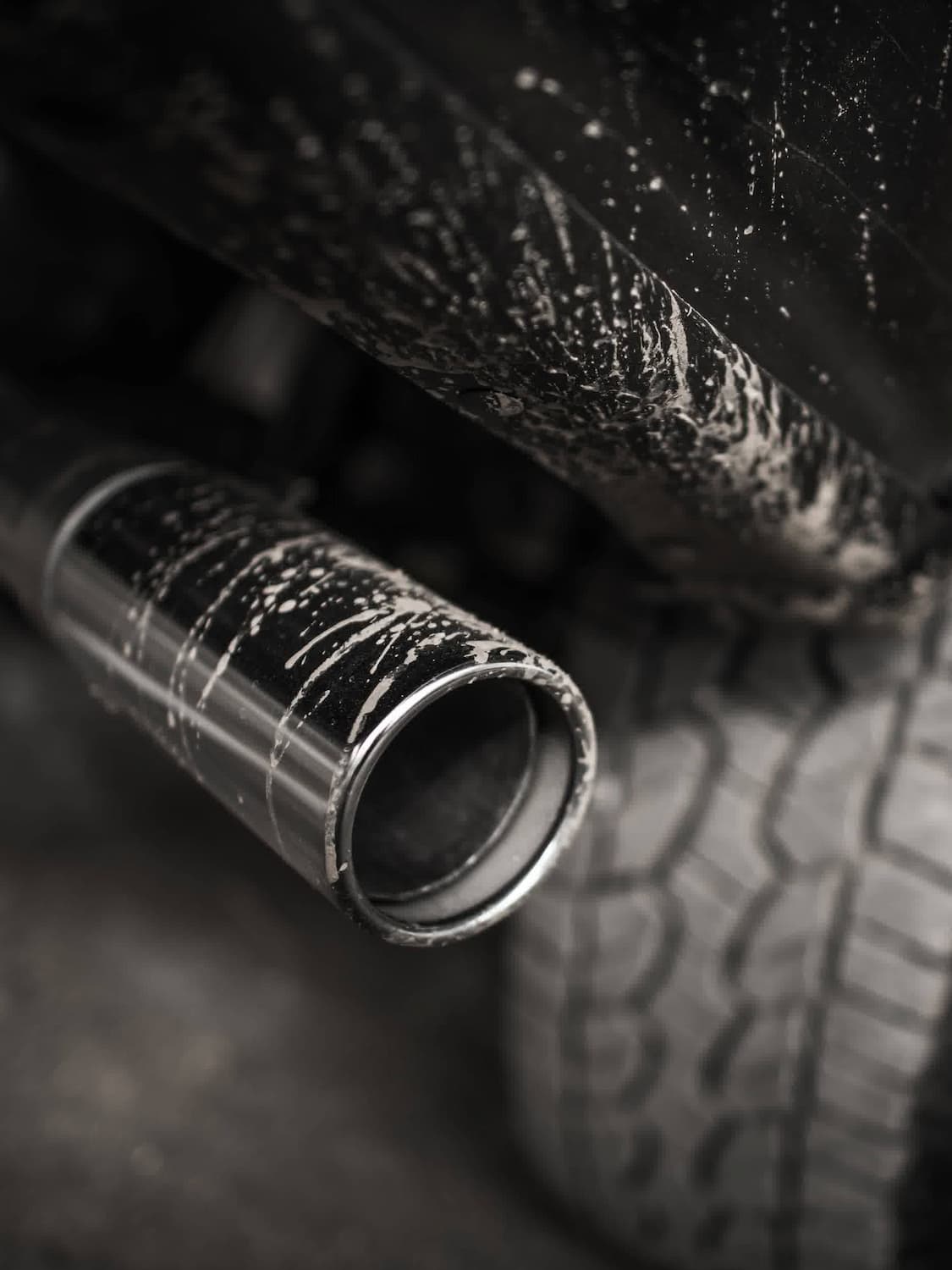 A close-up of a car’s exhaust pipe and rear tire, both covered in splattered mud, showing the vehicle’s underside and rugged use.